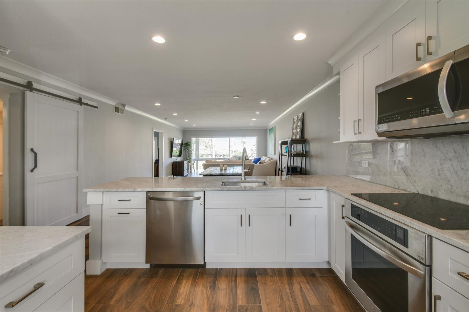 A modern kitchen with white cabinets, stainless steel appliances, and marble countertops overlooks a living area — 80 Celestial Way # 211, Juno Beach FL 33408, JUNO BEACH, FL