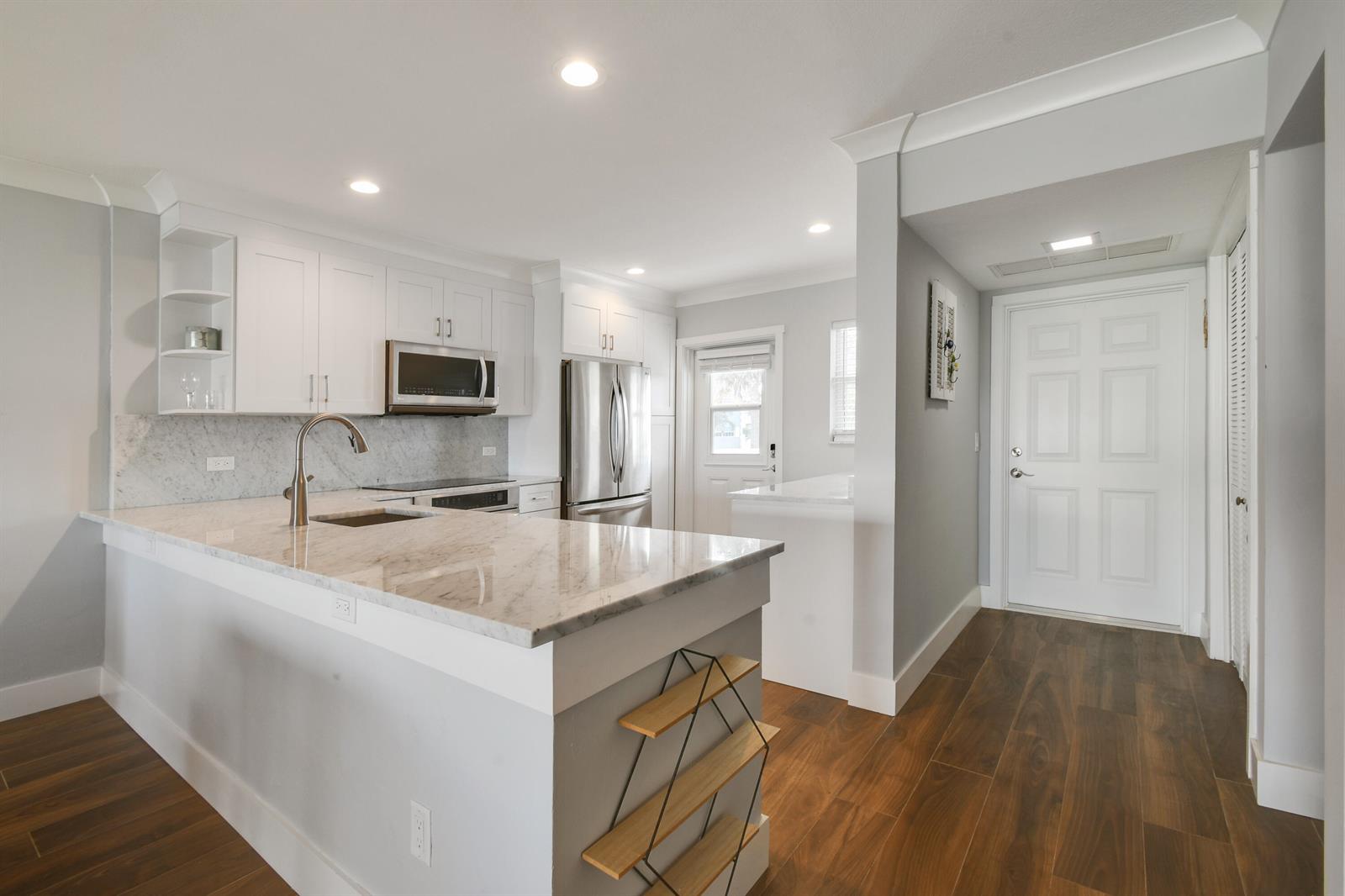 A modern kitchen features white cabinets, marble countertops, a breakfast bar, and wood-look flooring — 80 Celestial Way # 211, Juno Beach FL 33408, JUNO BEACH, FL
