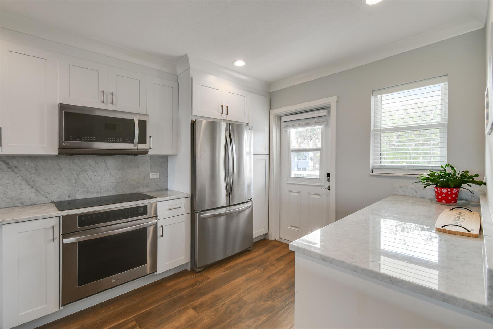 A kitchen with white cabinets, stainless steel appliances, marble countertops, and wood-look flooring — 80 Celestial Way # 211, Juno Beach FL 33408, JUNO BEACH, FL