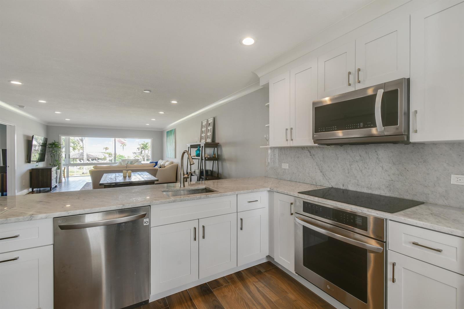 A modern kitchen with white cabinets, stainless steel appliances, and marble countertops overlooks a living area — 80 Celestial Way # 211, Juno Beach FL 33408, JUNO BEACH, FL