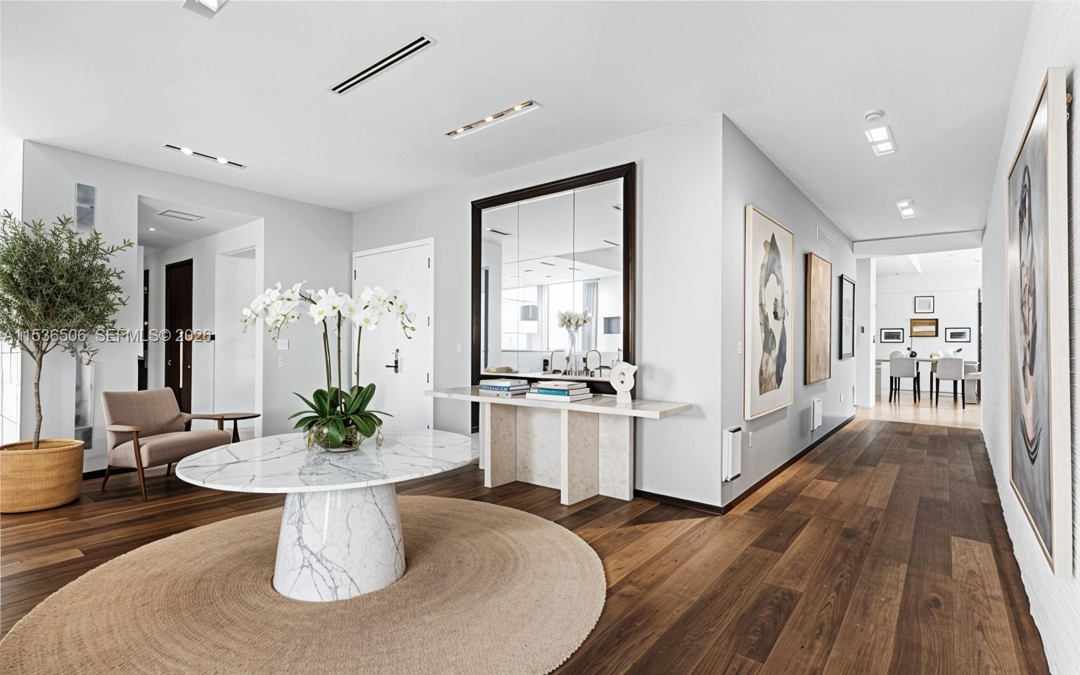 A modern foyer features a marble pedestal table, a large mirror, and hardwood flooring — 900 Brickell Key Blvd # 1002, Miami FL 33131, MIAMI, FL