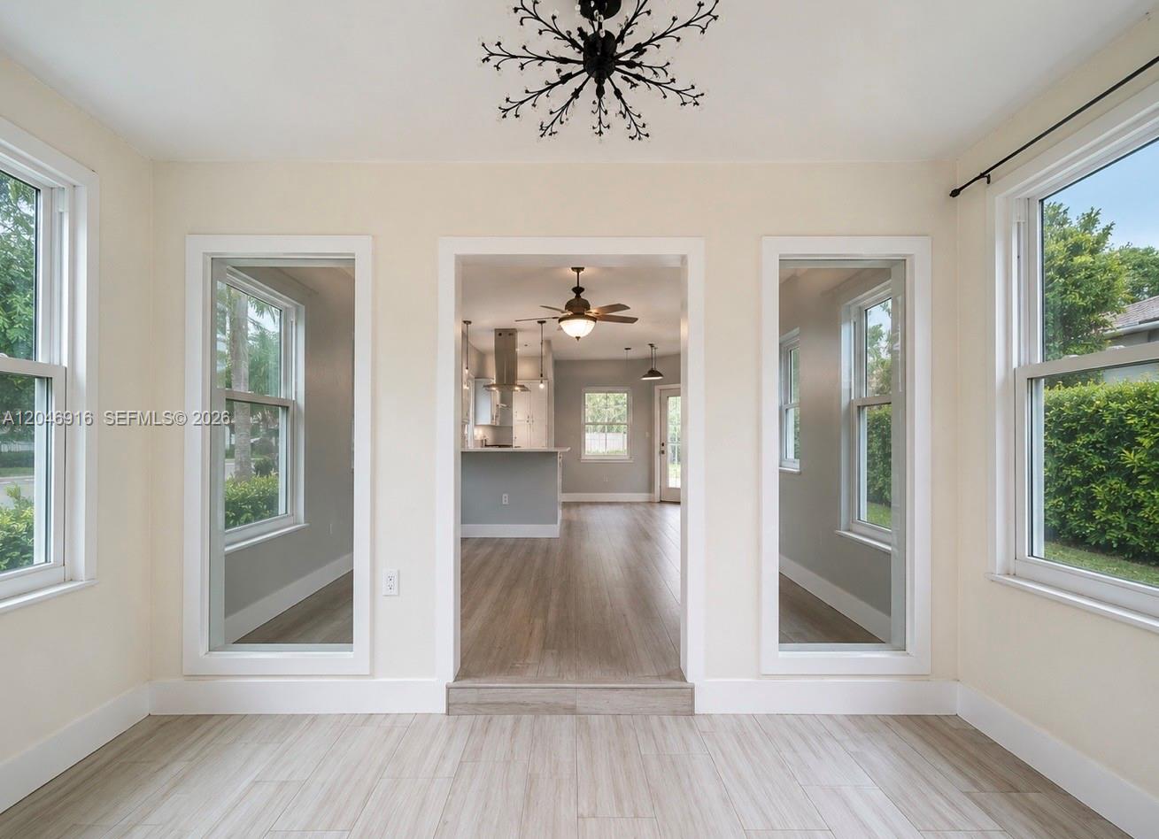 This sunroom features light wood-look flooring, a chandelier, and a doorway leading to a kitchen — 432 NW 103rd St # 1, Miami FL 33150, MIAMI, FL