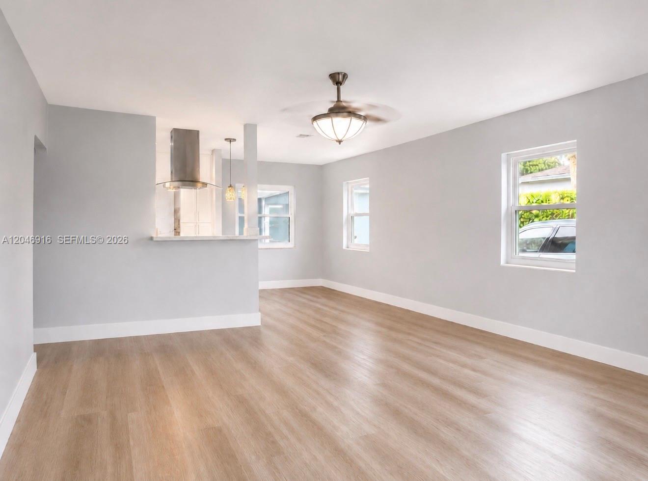 An empty room features light gray walls, wood-look flooring, a ceiling fan, and a kitchen pass-through — 432 NW 103rd St # 1, Miami FL 33150, MIAMI, FL