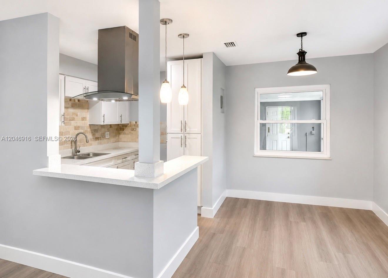 A kitchen with white cabinets, a breakfast bar, and a dining area with light flooring — 432 NW 103rd St # 1, Miami FL 33150, MIAMI, FL