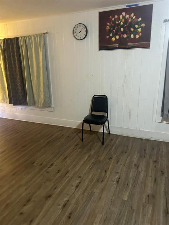 A room with wood-look flooring, white paneled walls, a single black chair, and a clock — 744 MYRTLE AVENUE, VENICE, FL
