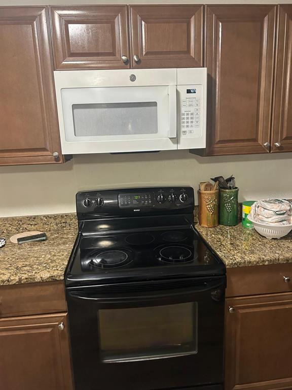 A kitchen features dark wood cabinets, a white over-the-range microwave, and a black electric stove — 744 MYRTLE AVENUE, VENICE, FL