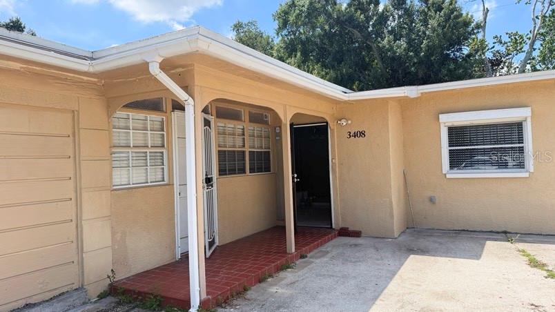 A tan stucco house exterior features a covered porch with red tile and white trim — 3408 W ELLICOTT STREET, TAMPA, FL