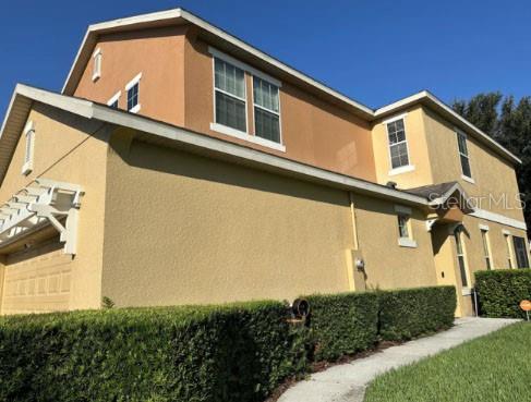 A low-angle exterior view of a two-story tan stucco house with a manicured hedge — 1338 GLENLEIGH DRIVE, OCOEE, FL