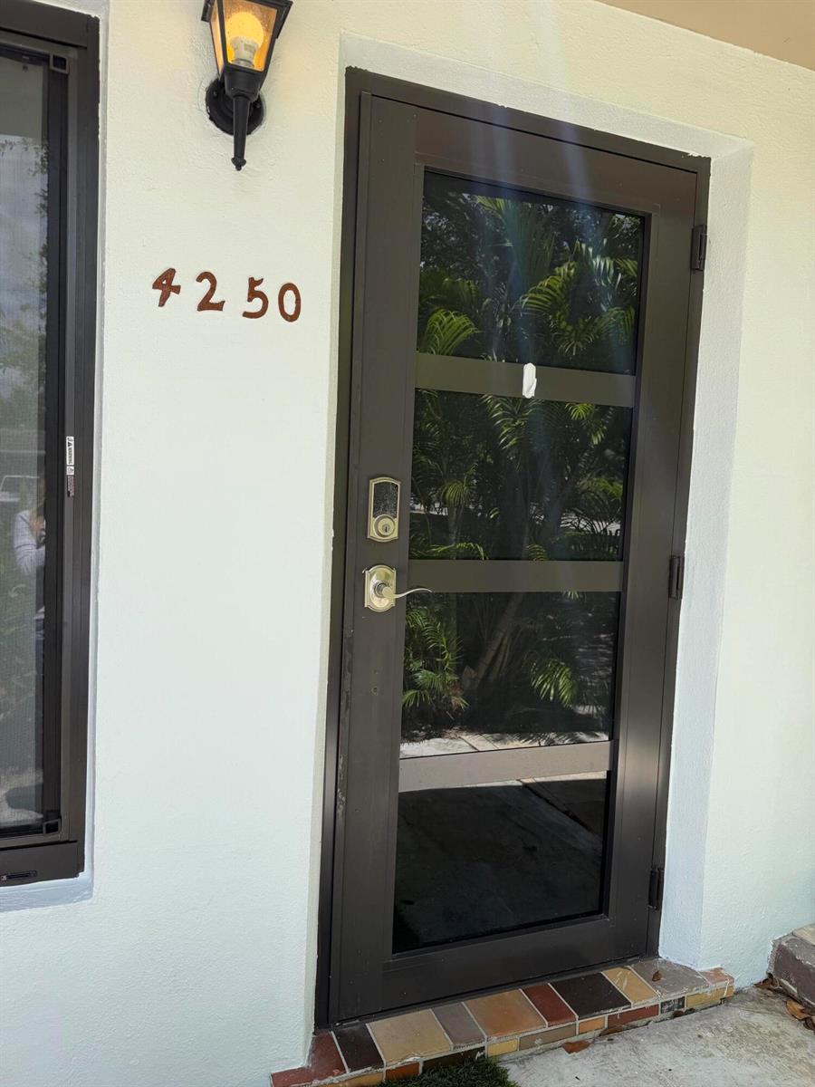 A dark-framed glass front door with a smart lock is mounted on a light-colored wall — 4250 NE 12th Avenue, Pompano Beach FL 33064, POMPANO BEACH, FL