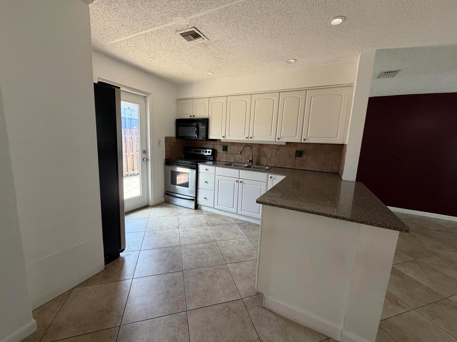 A kitchen features white cabinets, granite countertops, stainless steel appliances, and beige tile flooring — 4250 NE 12th Avenue, Pompano Beach FL 33064, POMPANO BEACH, FL