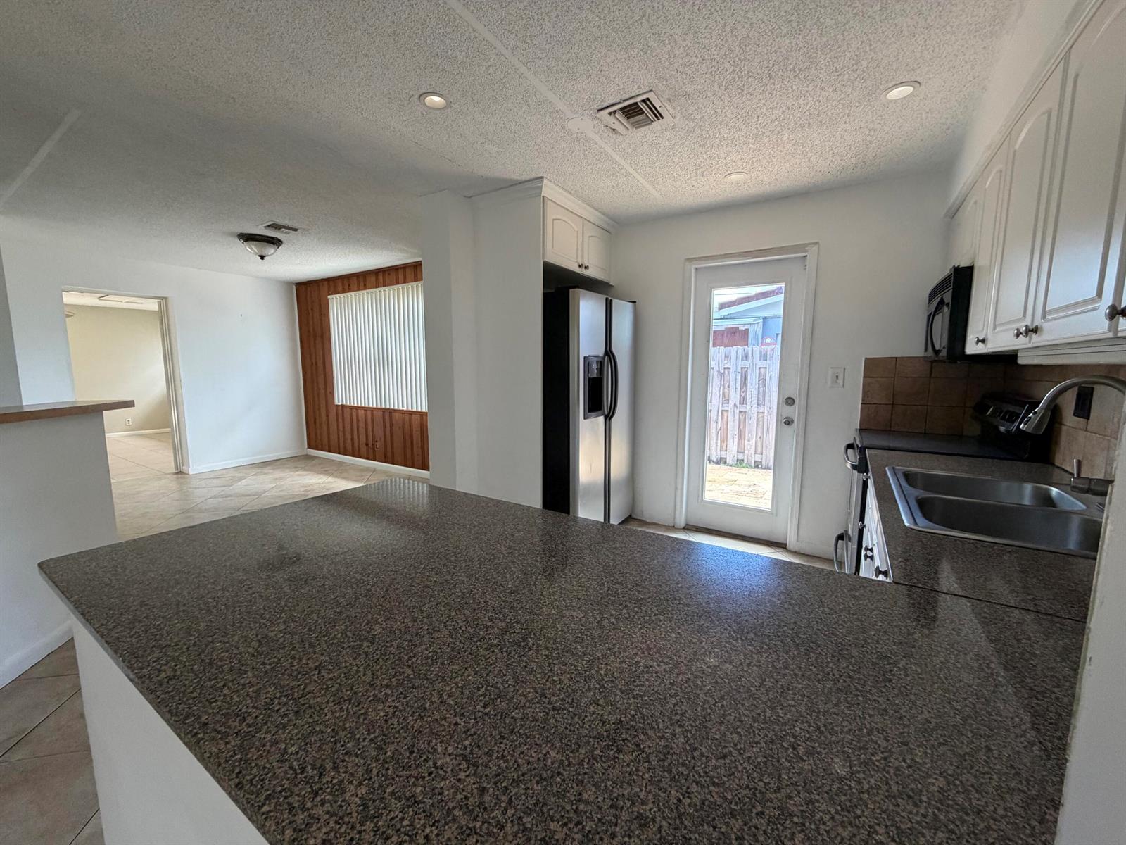 A kitchen with granite countertops, white cabinets, and a view into an adjacent living area — 4250 NE 12th Avenue, Pompano Beach FL 33064, POMPANO BEACH, FL