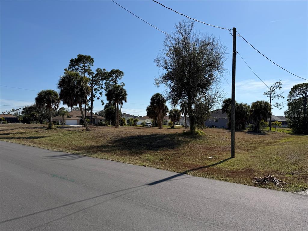 A vacant, grassy lot with several palm and deciduous trees sits beside a paved road — 2 PINE VALLEY CT, ROTONDA WEST, FL