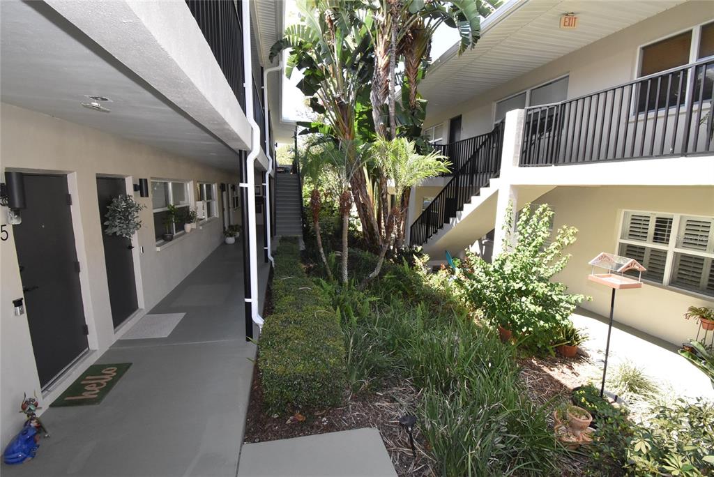 An outdoor walkway leads past apartment doors and a central garden area with stairs — 220 6TH AVENUE N UNIT 11, ST PETERSBURG, FL