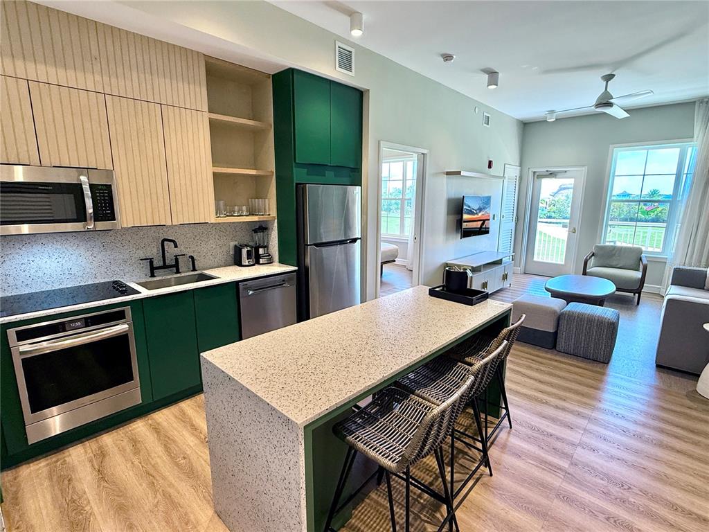 A modern kitchen with green cabinets and a stone island overlooks a living area — 3151 SUNSET WALK DRIVE UNIT 208, KISSIMMEE, FL