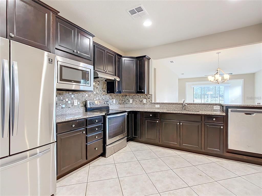 A kitchen with dark wood cabinets, stainless steel appliances, and granite countertops — 7732 SW 94TH CIRCLE, OCALA, FL