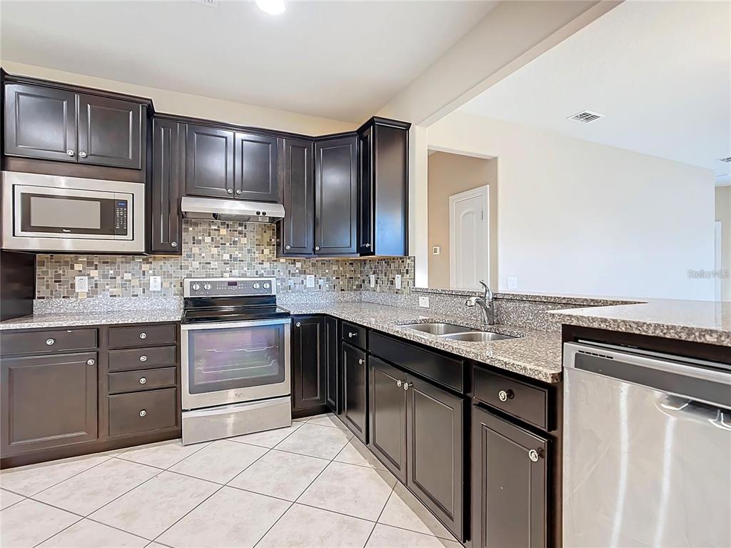 A kitchen features dark wood cabinets, granite countertops, a tiled backsplash, and stainless steel appliances — 7732 SW 94TH CIRCLE, OCALA, FL