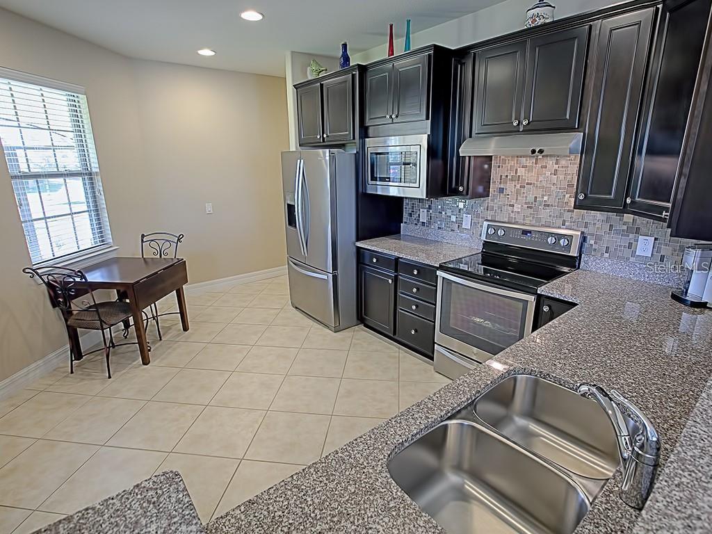 A kitchen with dark wood cabinets, granite countertops, stainless steel appliances, and a small dining area — 7732 SW 94TH CIRCLE, OCALA, FL