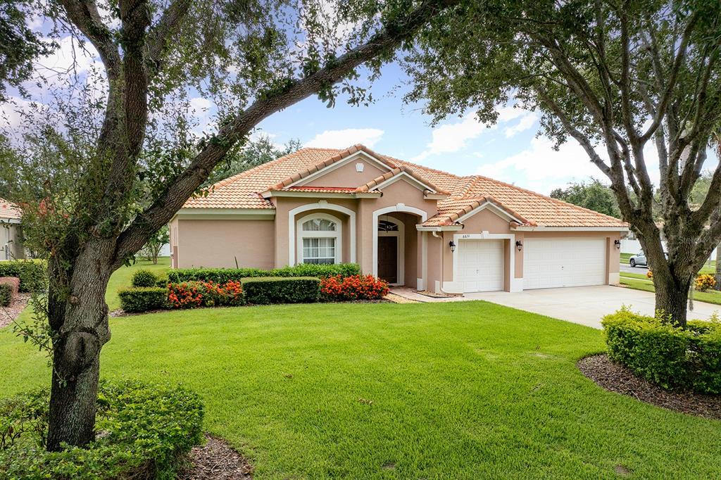 A single-story suburban house with a tan stucco exterior, tile roof, and a two-car garage — 6631 CRESTMONT GLEN LANE, WINDERMERE, FL
