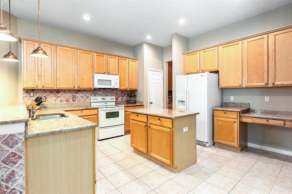 A kitchen features light wood cabinets, granite countertops, a central island, and white appliances — 6631 CRESTMONT GLEN LANE, WINDERMERE, FL