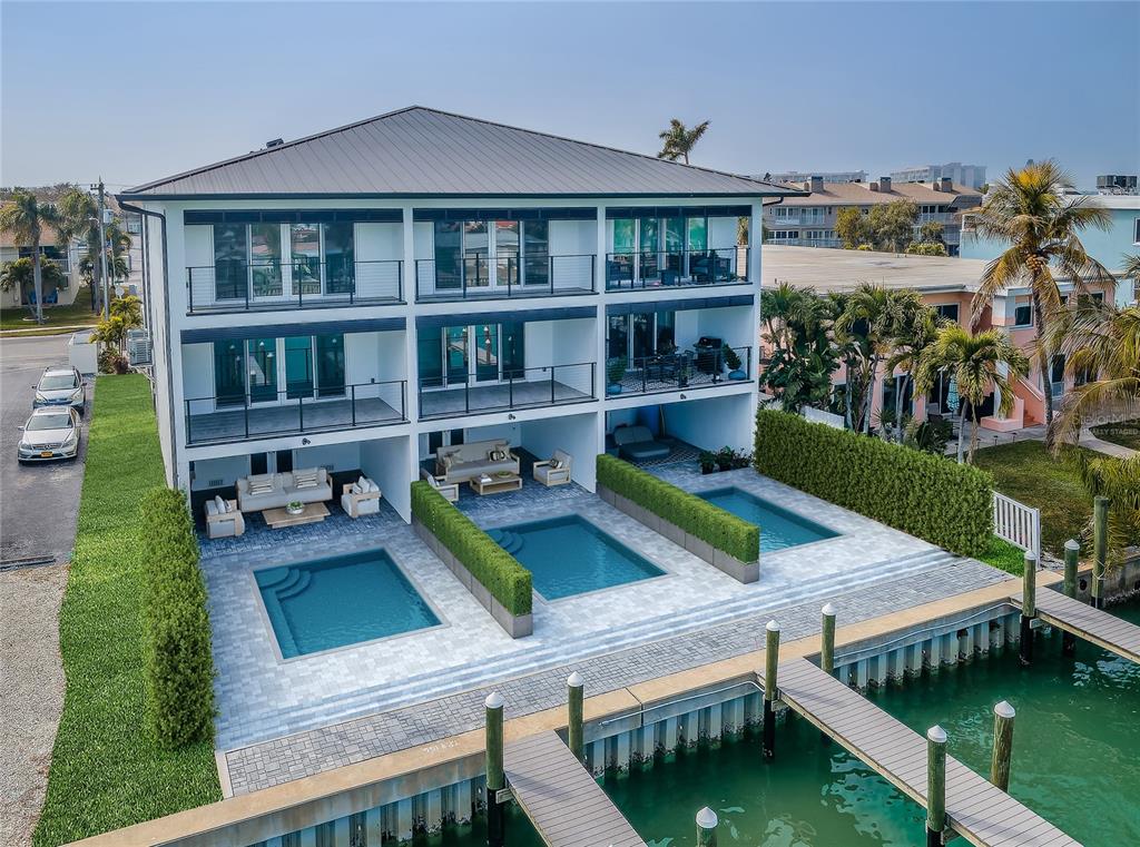An aerial view of a three-story waterfront building featuring private ground-level pools and boat docks — 12305 3RD STREET E UNIT 2, TREASURE ISLAND, FL