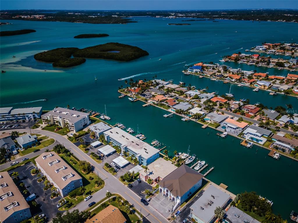 An aerial view shows waterfront residential buildings, boat docks, and a canal in Florida — 12305 3RD STREET E UNIT 2, TREASURE ISLAND, FL