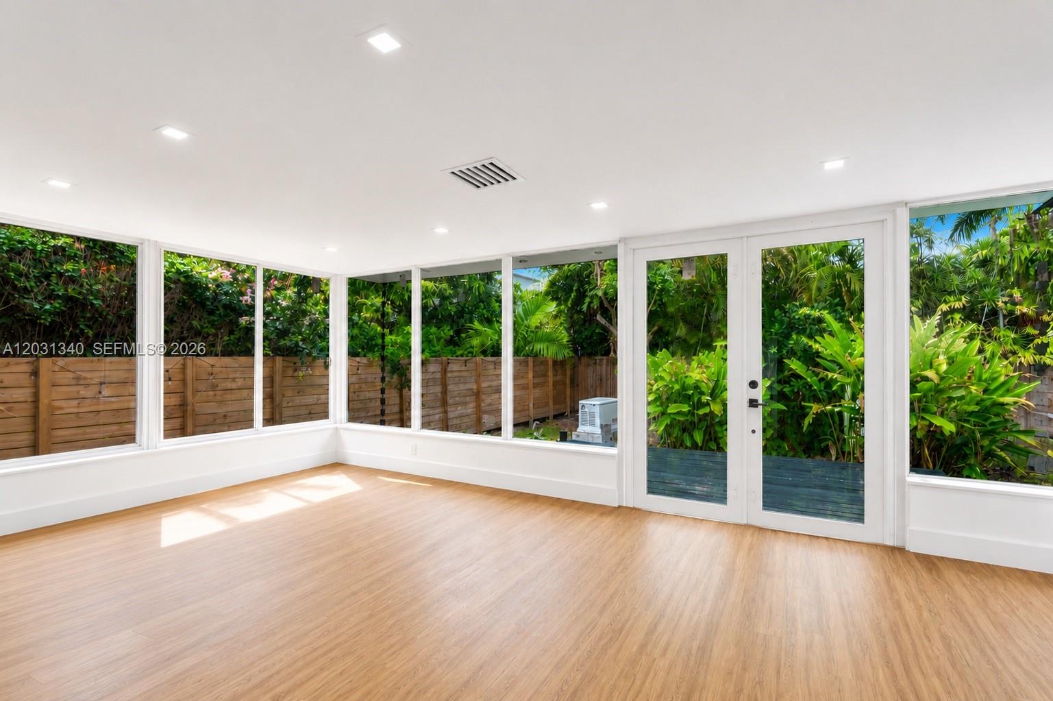 A sunroom with light wood flooring, white walls, recessed lighting, and large windows overlooking greenery — 8819 Dickens Ave, Surfside FL 33154, SURFSIDE, FL
