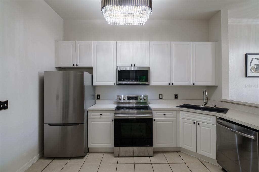 A kitchen features white cabinets, stainless steel appliances, a black sink, and tile flooring — 141 RESERVE CIRCLE UNIT 113, OVIEDO, FL