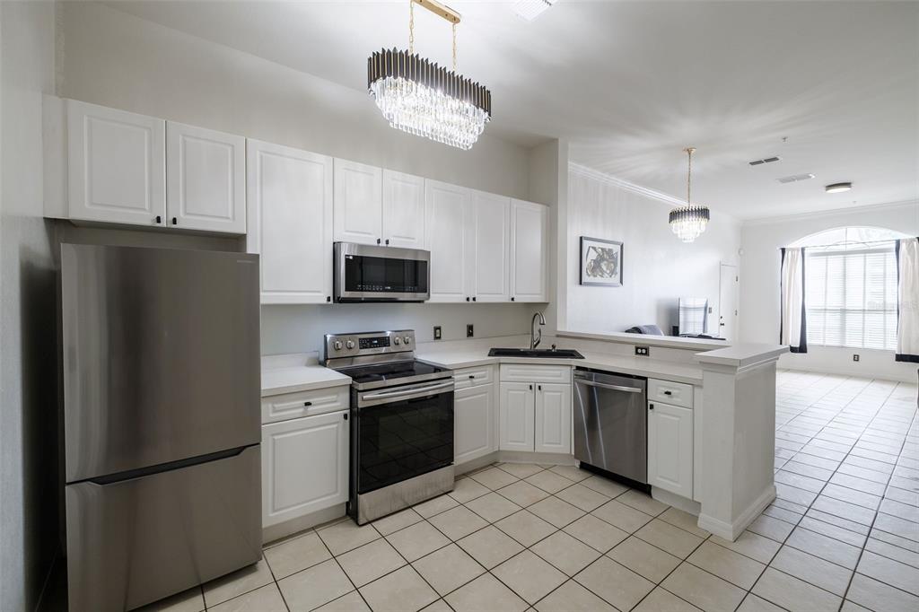 A kitchen with white cabinets, stainless steel appliances, and tile flooring opens to a living area — 141 RESERVE CIRCLE UNIT 113, OVIEDO, FL