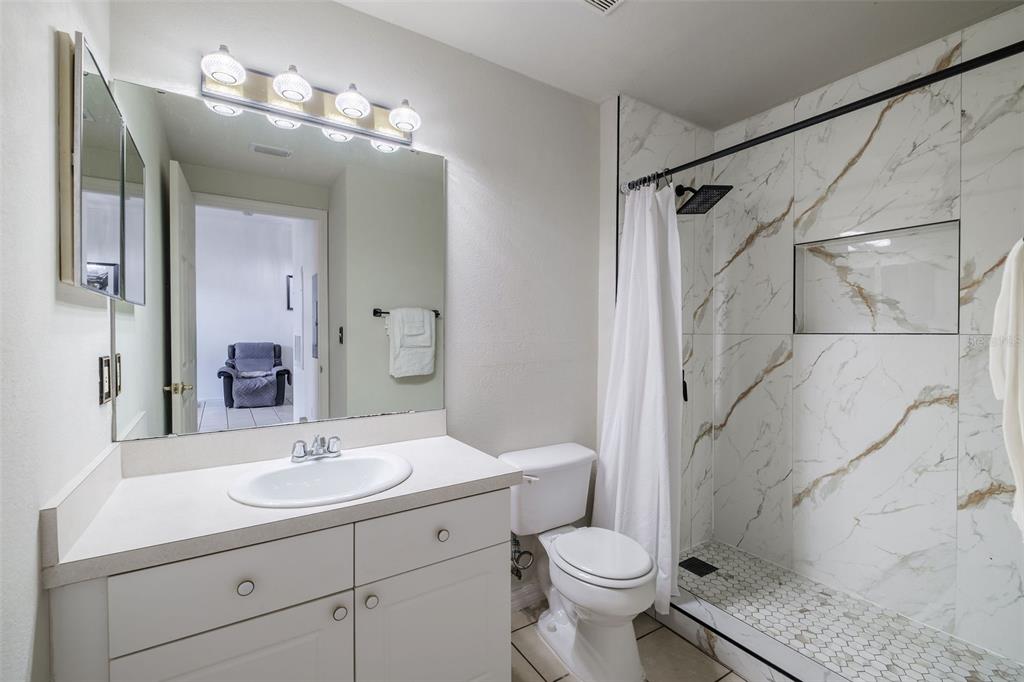A bathroom features a white vanity, a toilet, and a walk-in shower with marble-look tile — 141 RESERVE CIRCLE UNIT 113, OVIEDO, FL