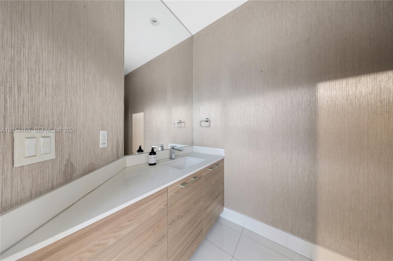 A modern bathroom features a wood-grain vanity, white countertop, and textured metallic-toned walls — 1300 S Miami Ave, Miami FL 33130, MIAMI, FL
