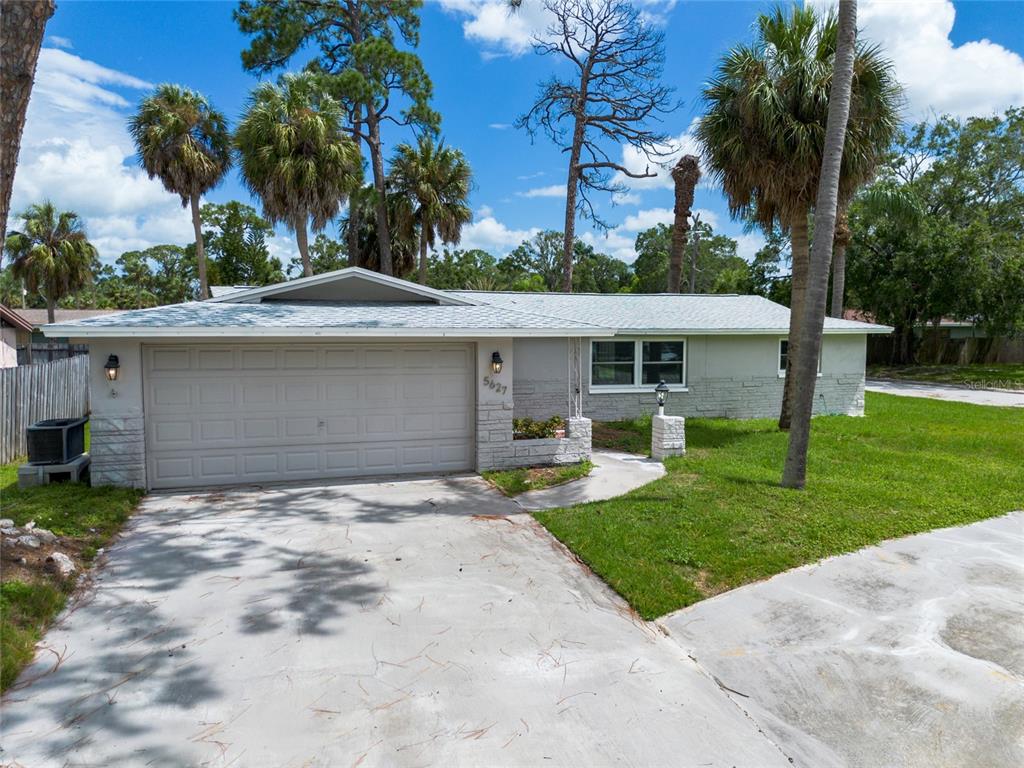 A single-story house with a gray garage door, stone accents, and palm trees in front — 5627 BERLIN DRIVE, PORT RICHEY, FL