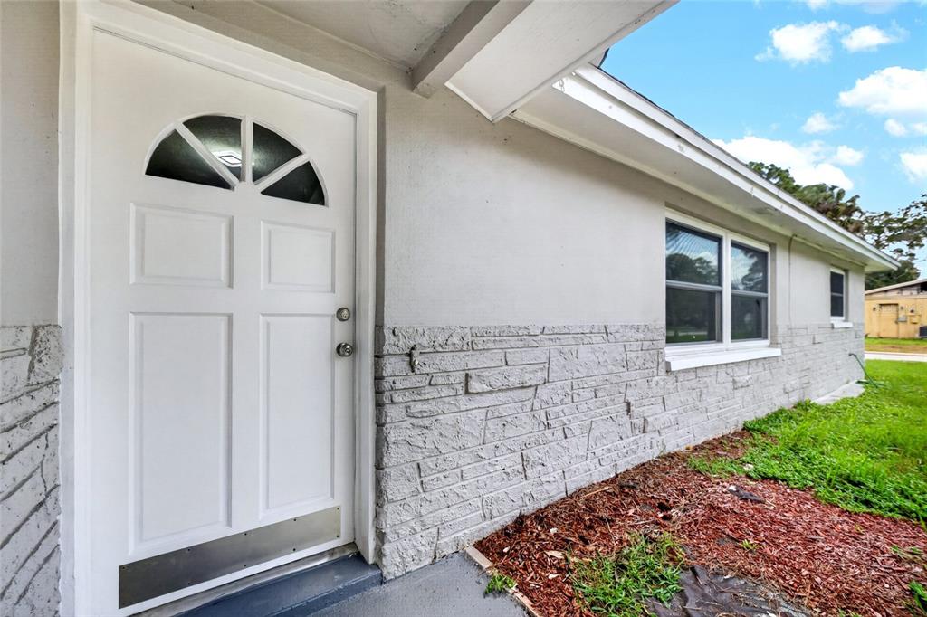 A white front door with a semi-circular window sits beside a gray stone-veneer wall — 5627 BERLIN DRIVE, PORT RICHEY, FL
