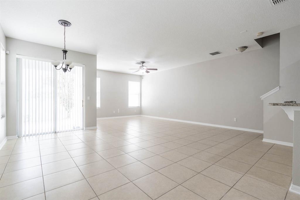 A spacious, open-concept living area features light-colored tile flooring, neutral walls, and sliding glass doors — 9326 WATCHET WAY, ORLANDO, FL
