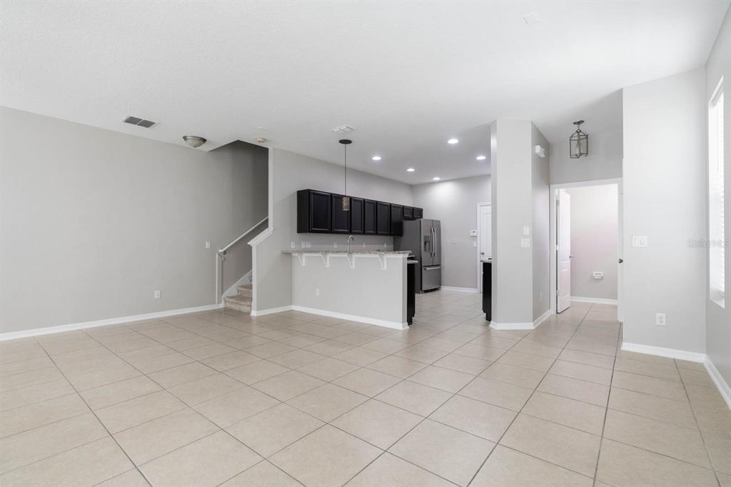 An open-concept living area features light tile flooring, a kitchen with dark cabinets, and stairs — 9326 WATCHET WAY, ORLANDO, FL