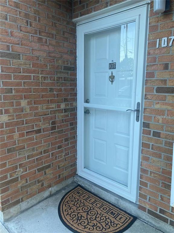 A white storm door with the number 107 is set into a brick exterior wall — 111 AIRPORT AVENUE W UNIT 107, VENICE, FL