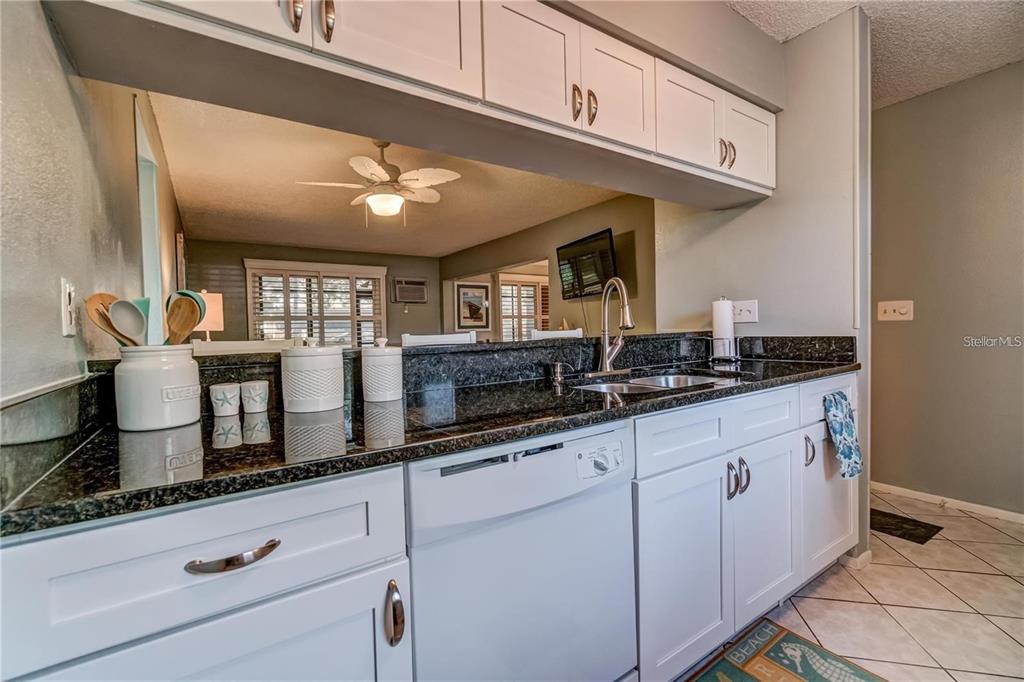 A kitchen features white cabinets, dark granite countertops, a dishwasher, and a pass-through window — 111 AIRPORT AVENUE W UNIT 107, VENICE, FL
