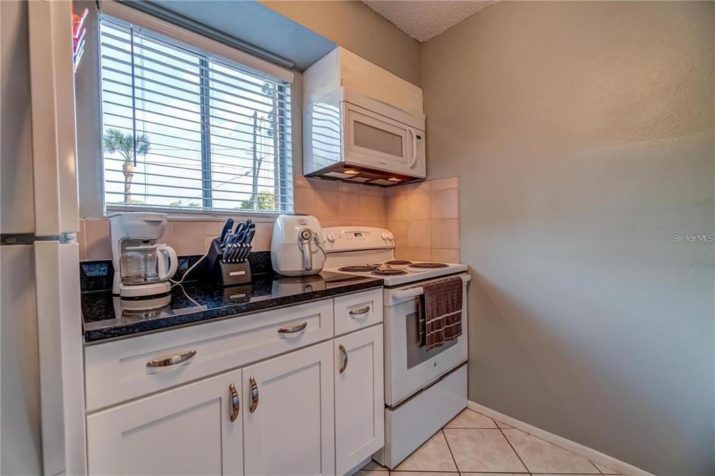 A kitchen features white cabinets, black countertops, a white stove, and a window with blinds — 111 AIRPORT AVENUE W UNIT 107, VENICE, FL