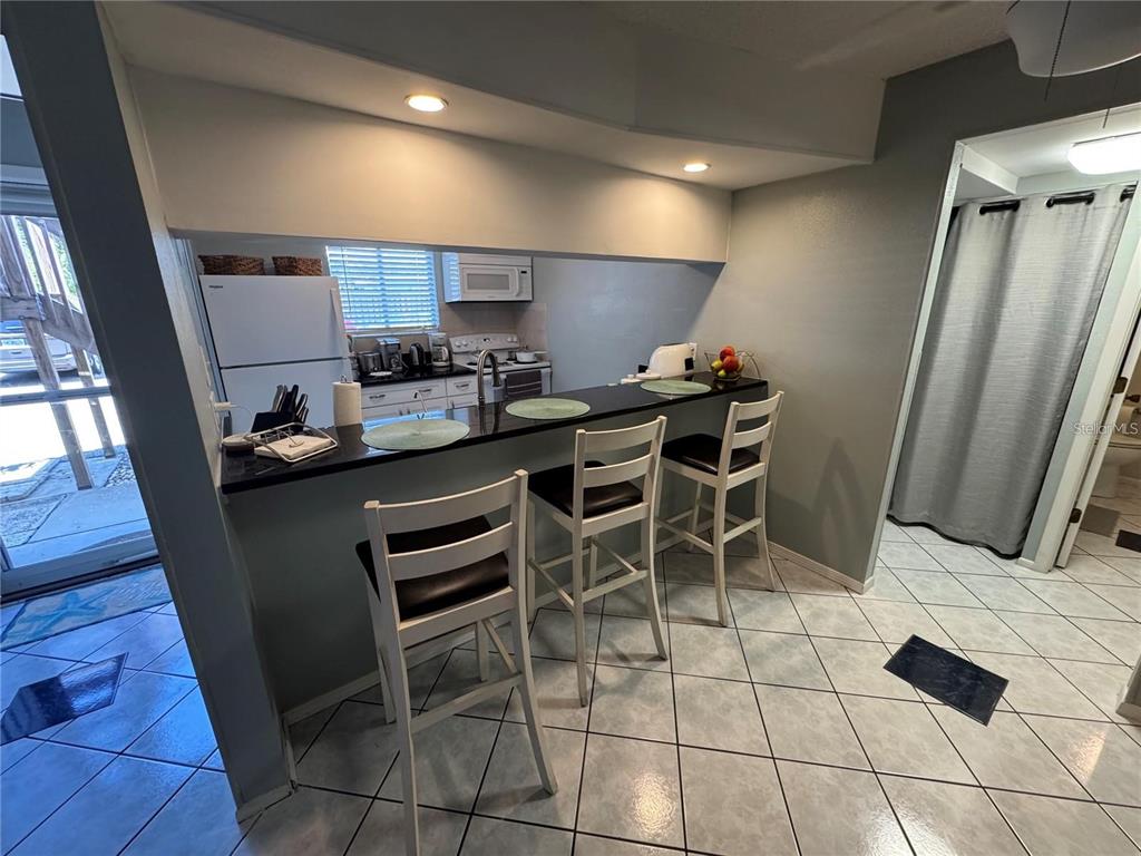A kitchen features a black breakfast bar with three chairs and white tile flooring — 111 AIRPORT AVENUE W UNIT 107, VENICE, FL