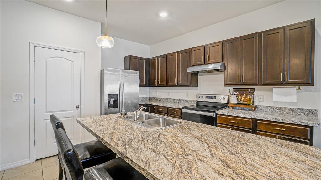 A kitchen features dark wood cabinets, granite countertops, stainless steel appliances, and a central island — 365 FELTRIM RESERVE BOULEVARD, DAVENPORT, FL