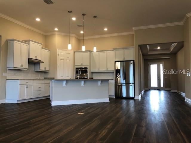 A kitchen features white cabinetry, a central island, stainless steel appliances, and dark wood flooring — 3181 AGOSTINO TERRACE, KISSIMMEE, FL