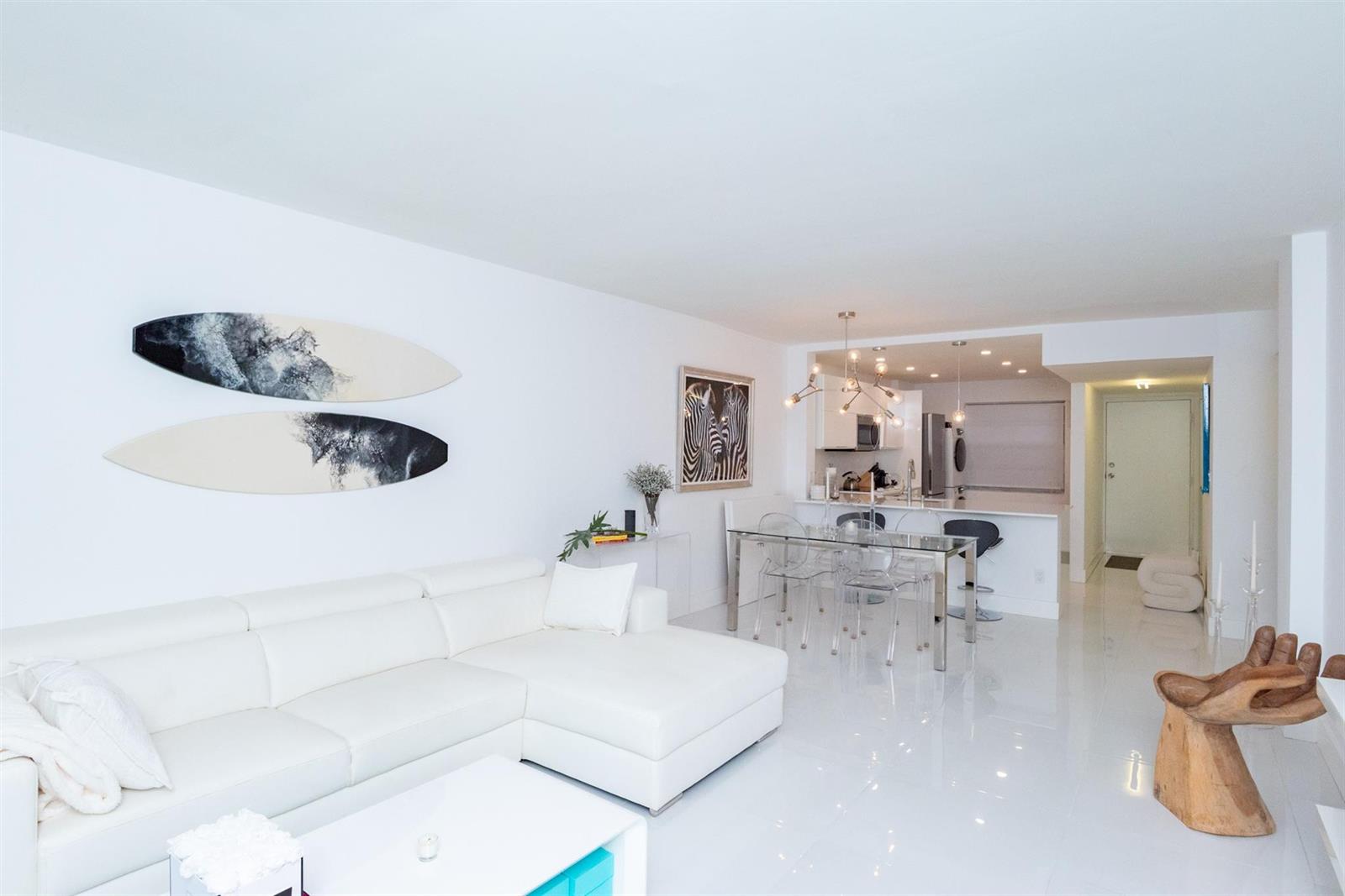 A bright living and dining area with white furniture, glossy floors, and surfboard wall art — 3581 S Ocean Boulevard # 2b, Palm Beach FL 33480, PALM BEACH, FL