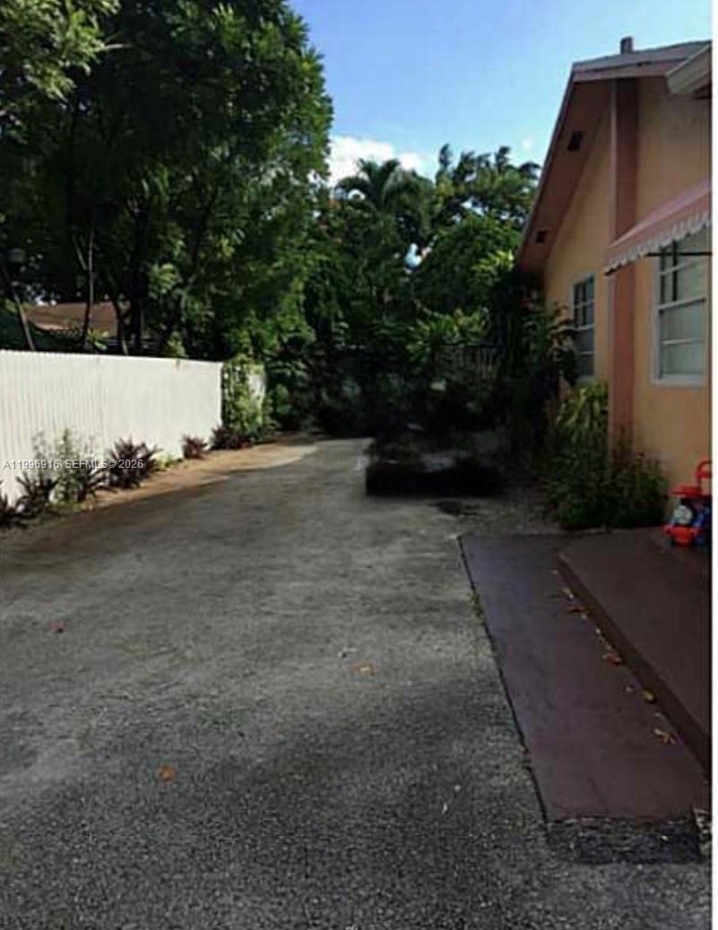 A concrete driveway runs alongside a tan house with a white fence and trees — 2528 SW 16th St, Miami FL 33145, MIAMI, FL