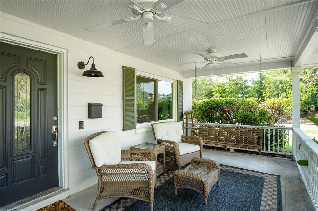 A covered front porch features wicker furniture, a hanging bench, and a dark front door — 501 MERIDALE AVENUE, ORLANDO, FL