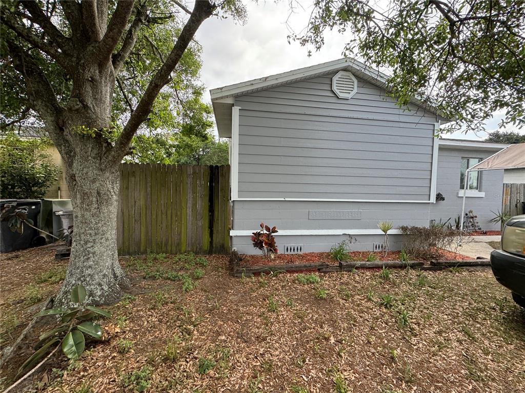 A gray house exterior features horizontal siding, a wooden fence, and a large tree — 3114 58TH AVENUE N, ST PETERSBURG, FL