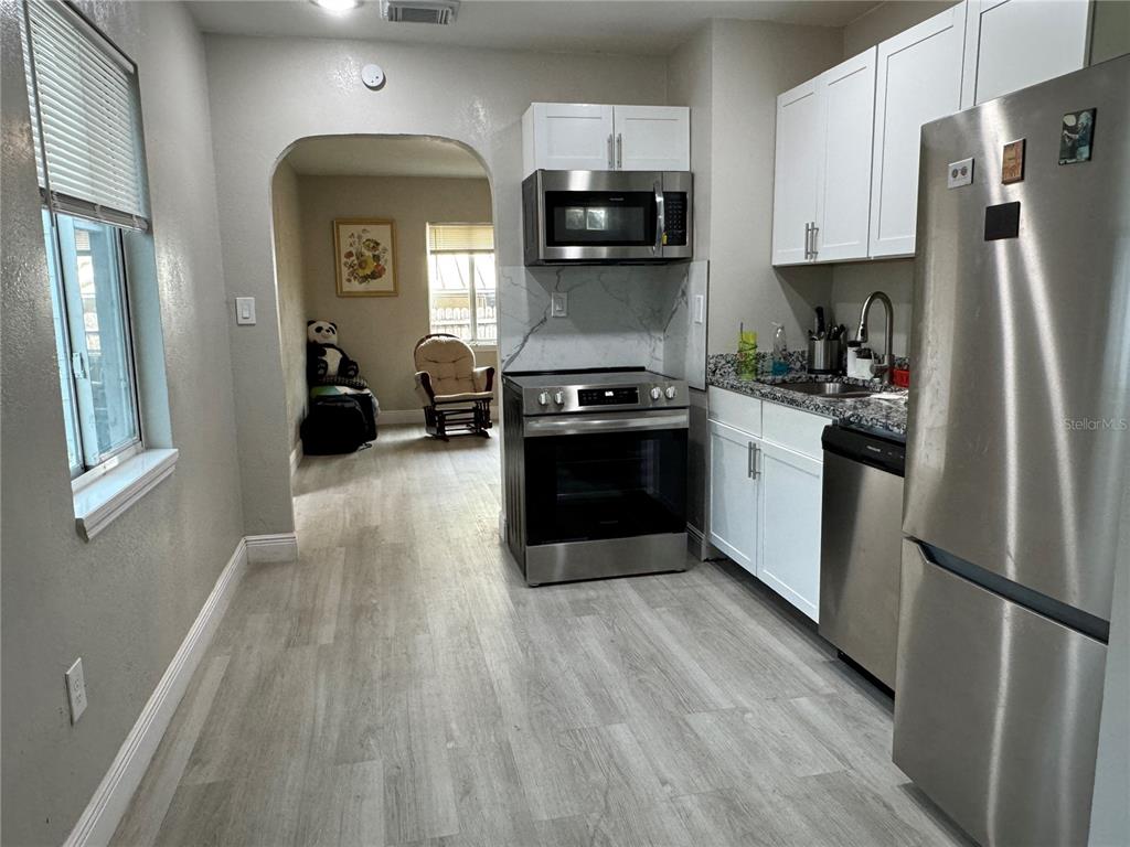A kitchen with stainless steel appliances, white cabinets, and light wood-look flooring leads to a living area — 3114 58TH AVENUE N, ST PETERSBURG, FL