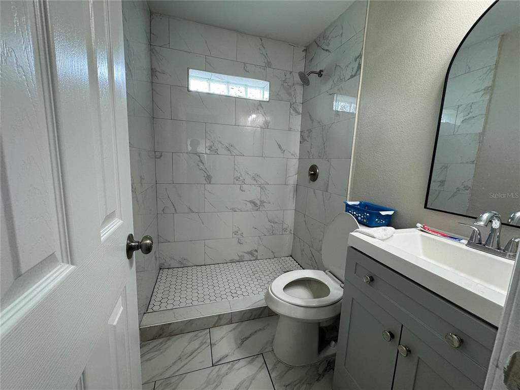 A bathroom features a walk-in shower with marble-look tile, a toilet, and a gray vanity — 3114 58TH AVENUE N, ST PETERSBURG, FL