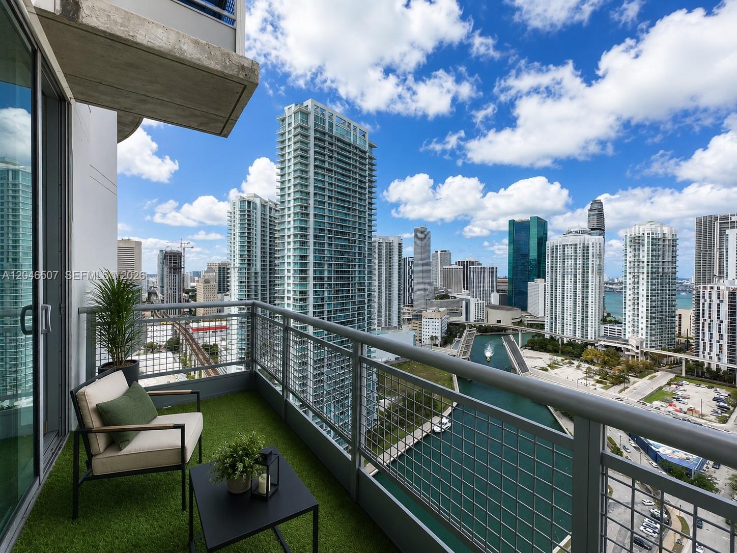 A balcony with artificial turf, a chair, and a table overlooks a city skyline and river — 690 SW 1st Ct # 3104, Miami FL 33130, MIAMI, FL