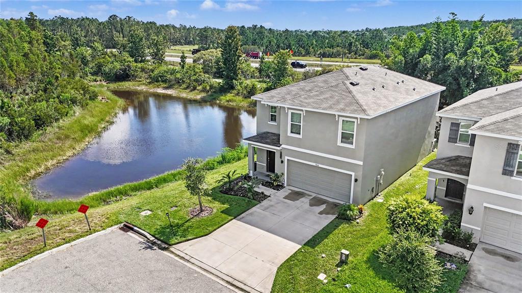 An aerial view shows a two-story house with a concrete driveway next to a pond — 3446 SUNCOAST PLAINS DRIVE, ODESSA, FL