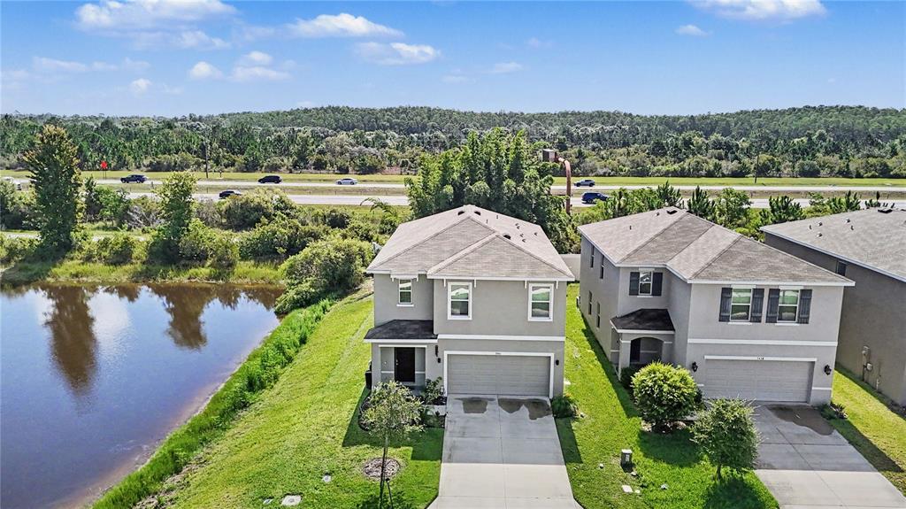 An aerial view shows two suburban houses next to a pond and a highway — 3446 SUNCOAST PLAINS DRIVE, ODESSA, FL