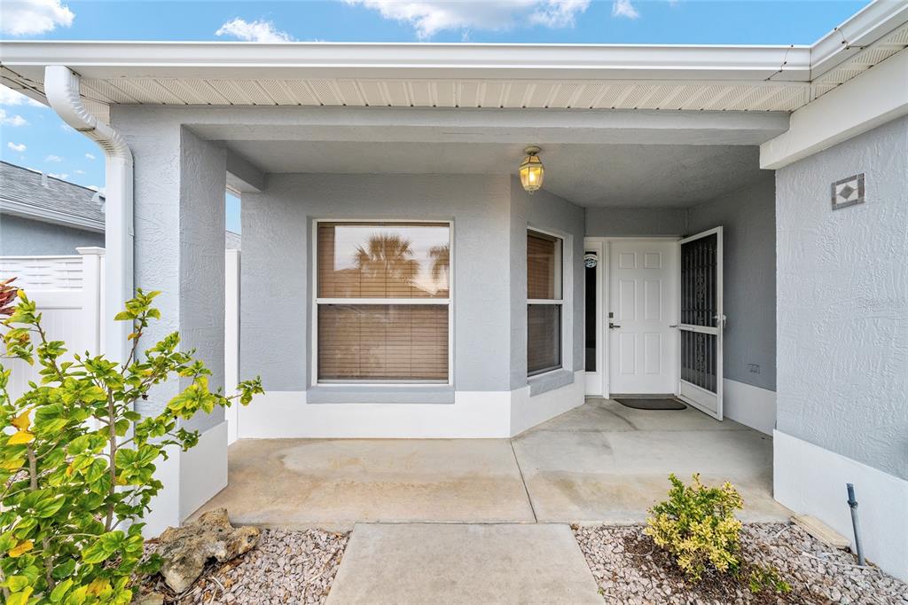 A covered concrete porch leads to a white front door with a screen door — 1928 PEACHTREE AVENUE, THE VILLAGES, FL